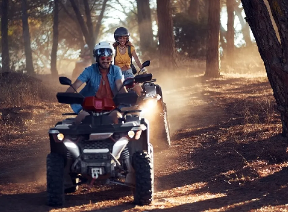 A man and a woman driving an ATV in the forest