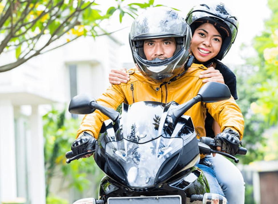 Two people sitting on a motorcycle wearing helmets and smiling